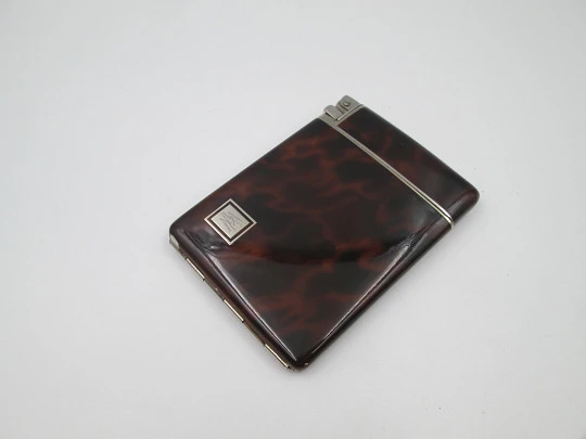 Inusual encendedor automático a gasolina con pitillera Dios. Metal plateado y esmalte carey