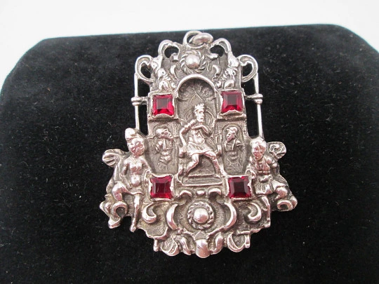 Medalla colgante pórtico. Plata de ley y granates. Escena relieve rey con querubines