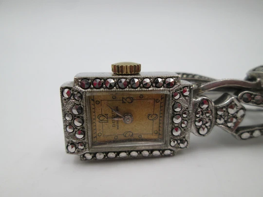 Reloj colgante Dulux. Metal rodiado. Cuerda. Lazo plata. Marquesitas. 1950