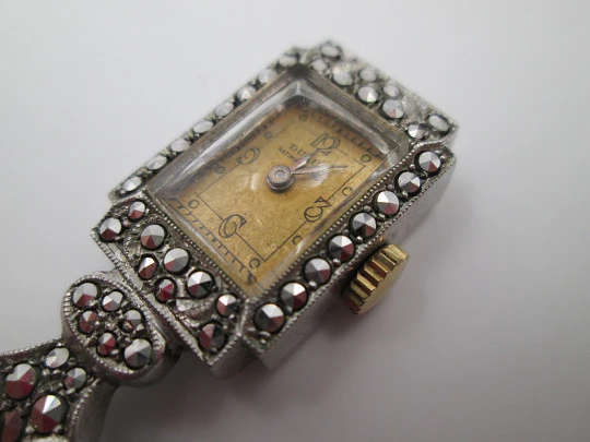 Reloj colgante Dulux. Metal rodiado. Cuerda. Lazo plata. Marquesitas. 1950