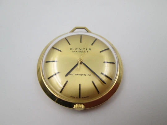 Reloj colgante Kienzle Markant. Metal chapado oro. Cuerda manual. Alemania. 1960