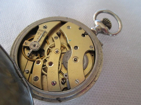Reloj francés de alpaca. Remontoir con pulsador. 1910. Fondo decorado